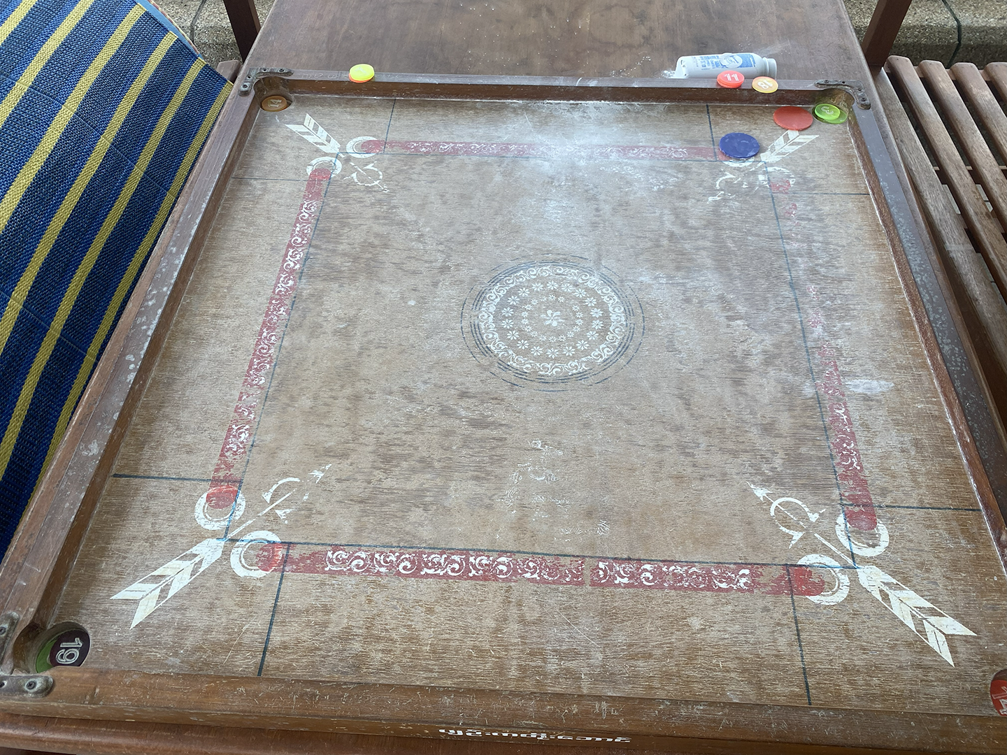 Picture of a popular Southern Asia board game, named Carrom, with colored discs on the board and small holes/pockets in the corners